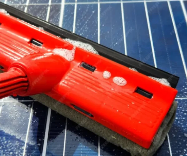 Technician gently cleaning rooftop solar panels with soft brush and water